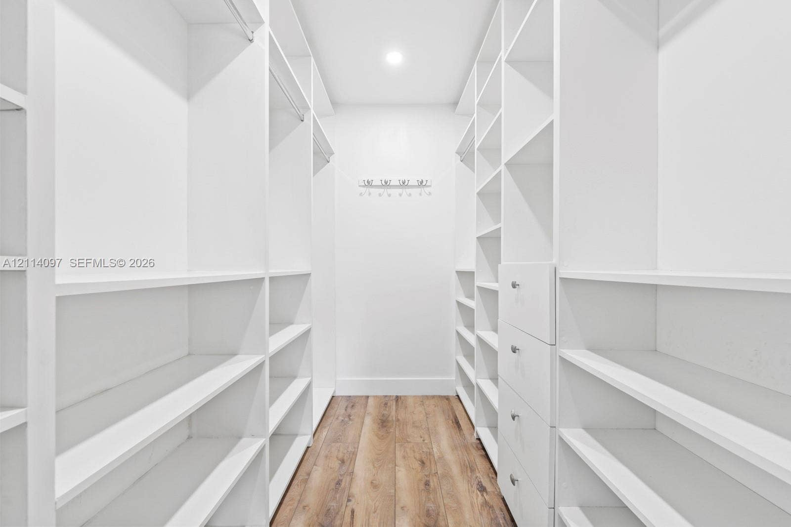 7905 SW 104th Street, #206H, Miami, FL 33156 Walk-in closet featuring white built-in shelving, integrated garment rods, custom drawer storage, and wood-finish flooring