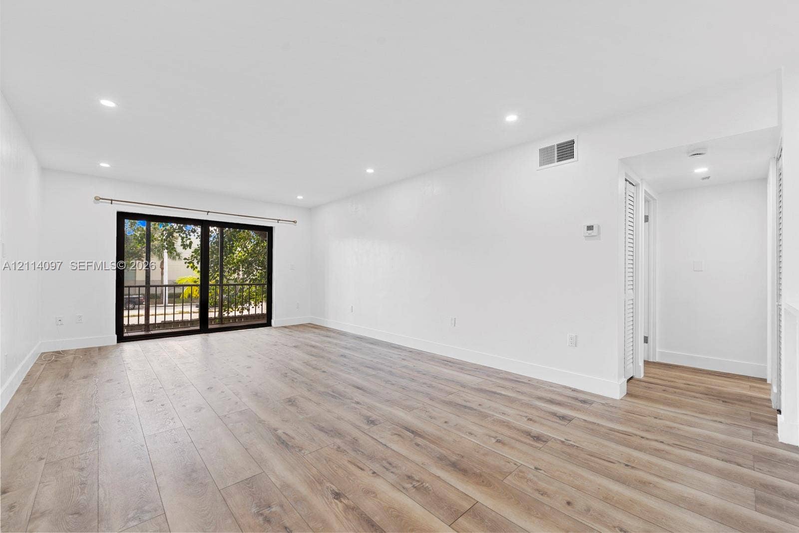7905 SW 104th Street, #206H, Miami, FL 33156 Open interior featuring wood-finish flooring, recessed lighting, and large sliding glass doors with black framing