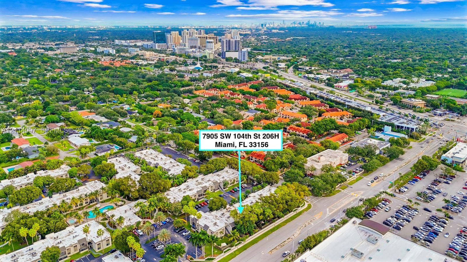 7905 SW 104th Street, #206H, Miami, FL 33156 Aerial perspective of residential community featuring low-rise multi-family structures, mature tree canopy, integrated parking areas, and proximity to regional infrastructure and urban skyline