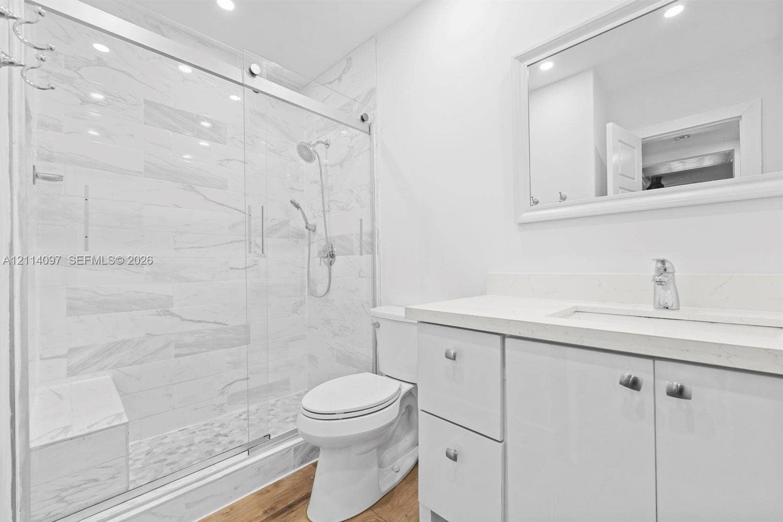 7905 SW 104th Street, #206H, Miami, FL 33156 Bathroom featuring a walk-in shower with glass sliding doors, built-in tiled bench, stone-patterned wall tile, vanity with a light-toned countertop, and wood-finish flooring
