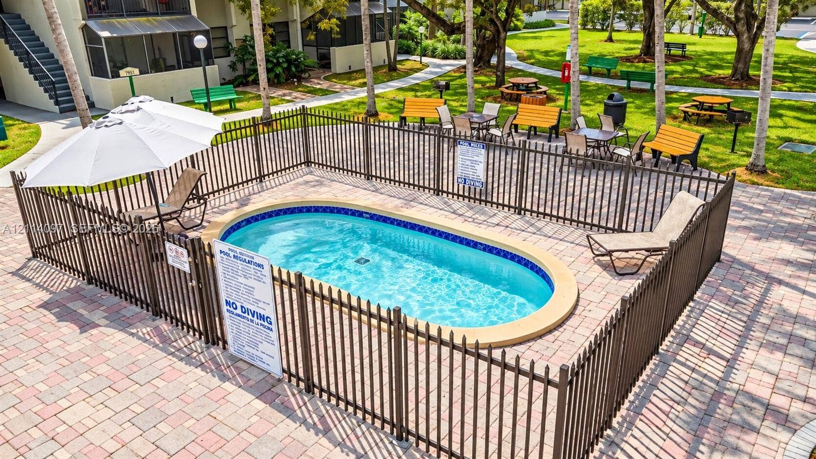 7905 SW 104th Street, #206H, Miami, FL 33156 Oval swimming pool featuring a decorative tile border, surround fencing, and a paver stone deck