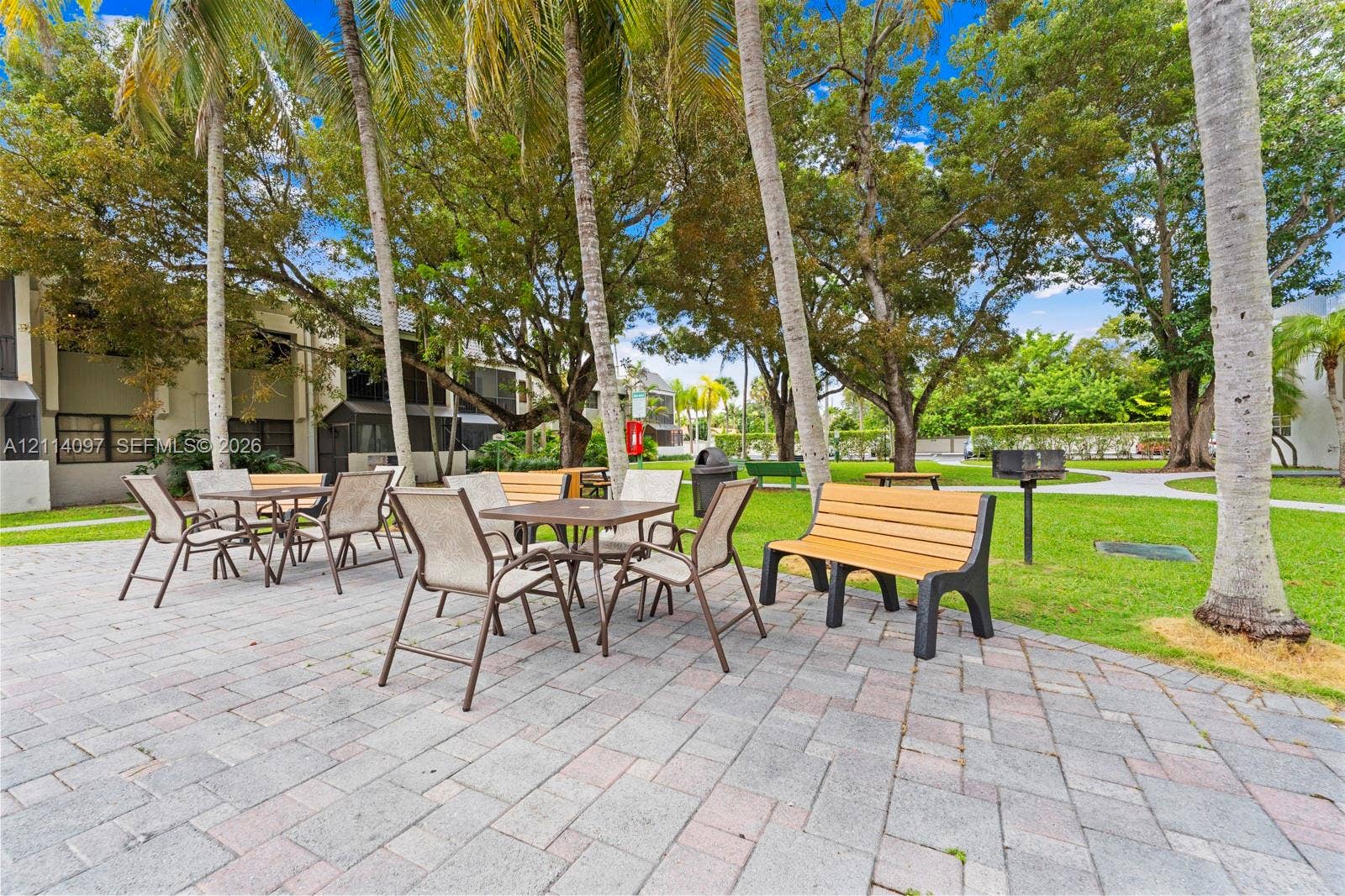 7905 SW 104th Street, #206H, Miami, FL 33156 Outdoor recreation area featuring a paved stone patio, built-in pedestal grill, and mature palms set within a landscaped lawn