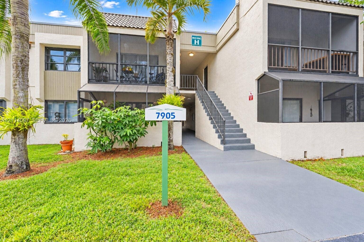 7905 SW 104th Street, #206H, Miami, FL 33156 Multi-level stucco exterior featuring screened balconies, covered staircase with metal railing, and paved entry walkway