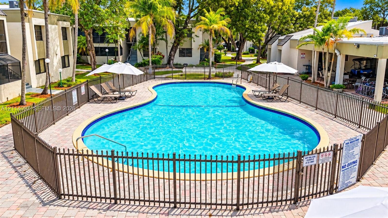 7905 SW 104th Street, #206H, Miami, FL 33156 Community swimming pool featuring a paved deck, perimeter metal fencing, and surrounding mature palm trees