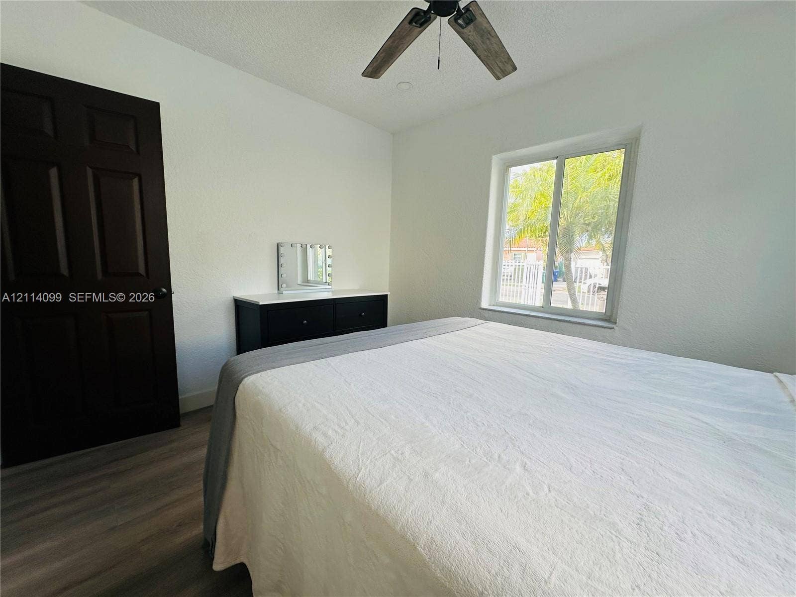 3052 SW 6th Street, Miami, FL 33135 Room featuring wood-finish flooring, a dark-toned solid core door, and a ceiling fan with integrated lighting