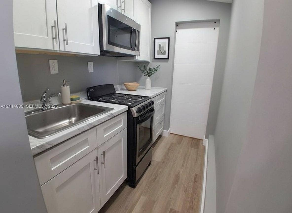 3052 SW 6th Street, Miami, FL 33135 Kitchen featuring white shaker-style cabinetry, stone-finish countertops, stainless steel appliances, a stainless steel sink, and wood-finish flooring