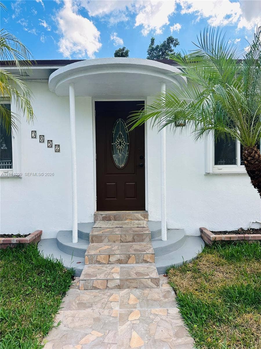 3052 SW 6th Street, Miami, FL 33135 Exterior entrance featuring a covered circular portico with dual structural columns, stone-tile walkway and steps, and a solid-panel door with an oval glass insert