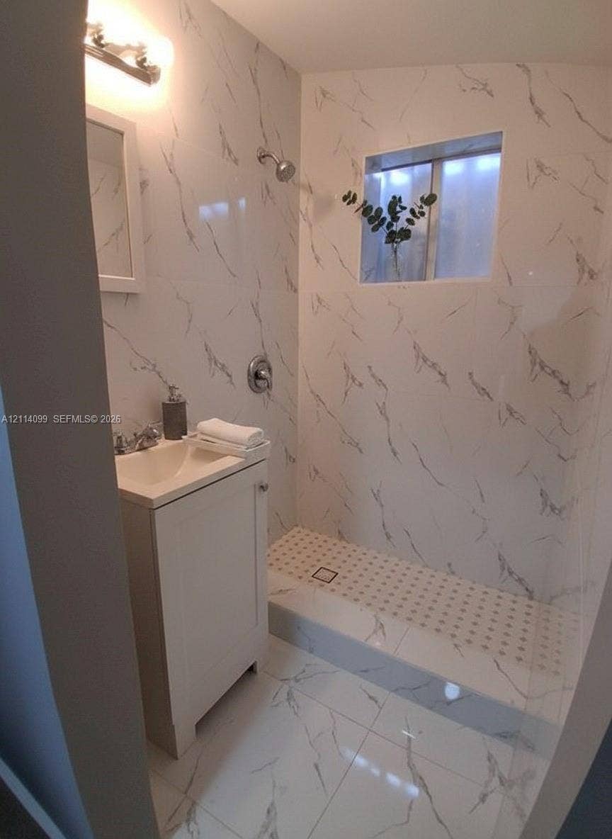 3052 SW 6th Street, Miami, FL 33135 Full-height wall tiling with a veined pattern, walk-in shower with a low-profile threshold, high-gloss floor tiling, vanity cabinet with a integrated sink, and wall-mounted vanity lighting