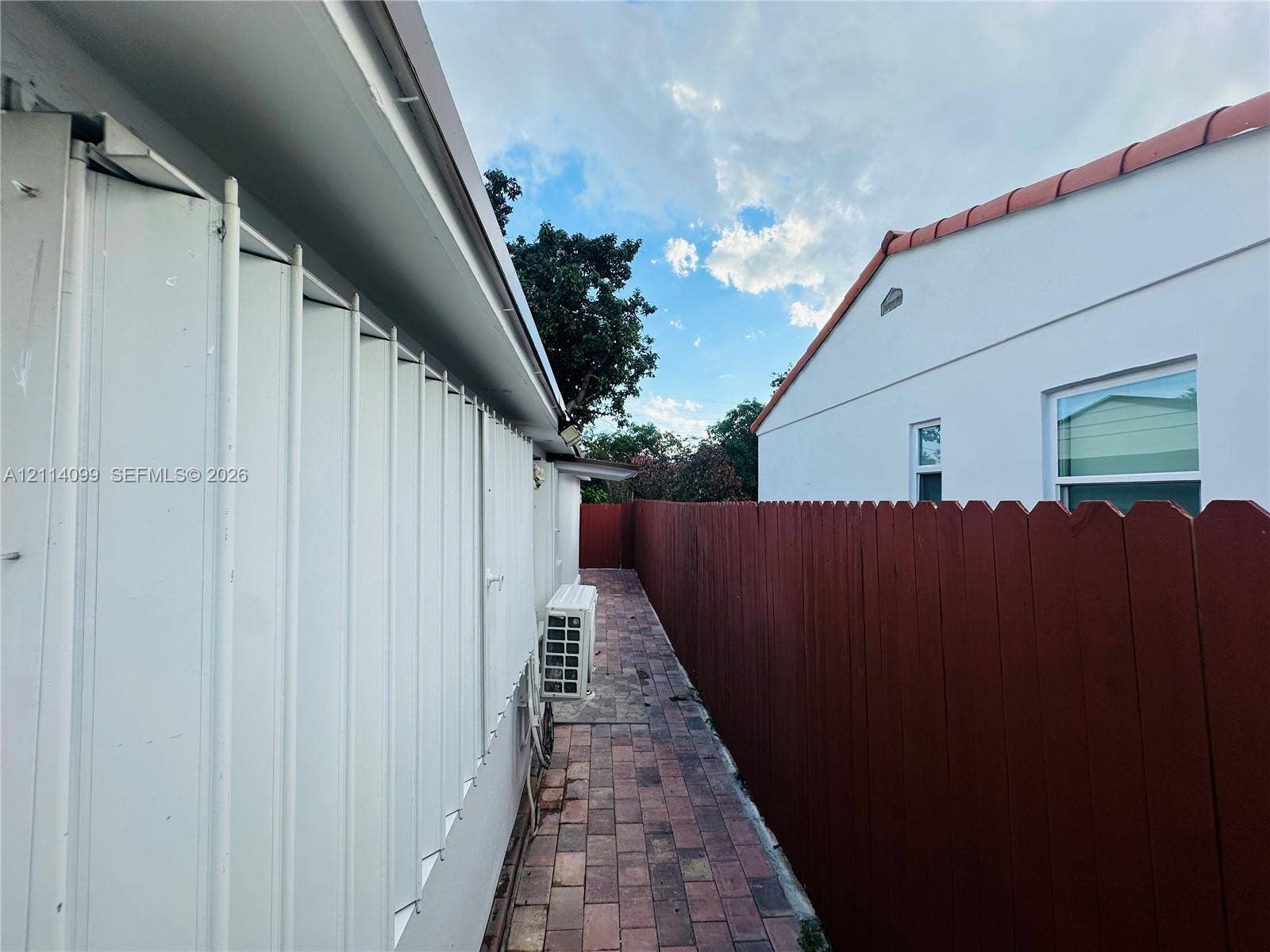 3052 SW 6th Street, Miami, FL 33135 Exterior side walkway featuring brick paver flooring, vertical siding, and a wood privacy fence