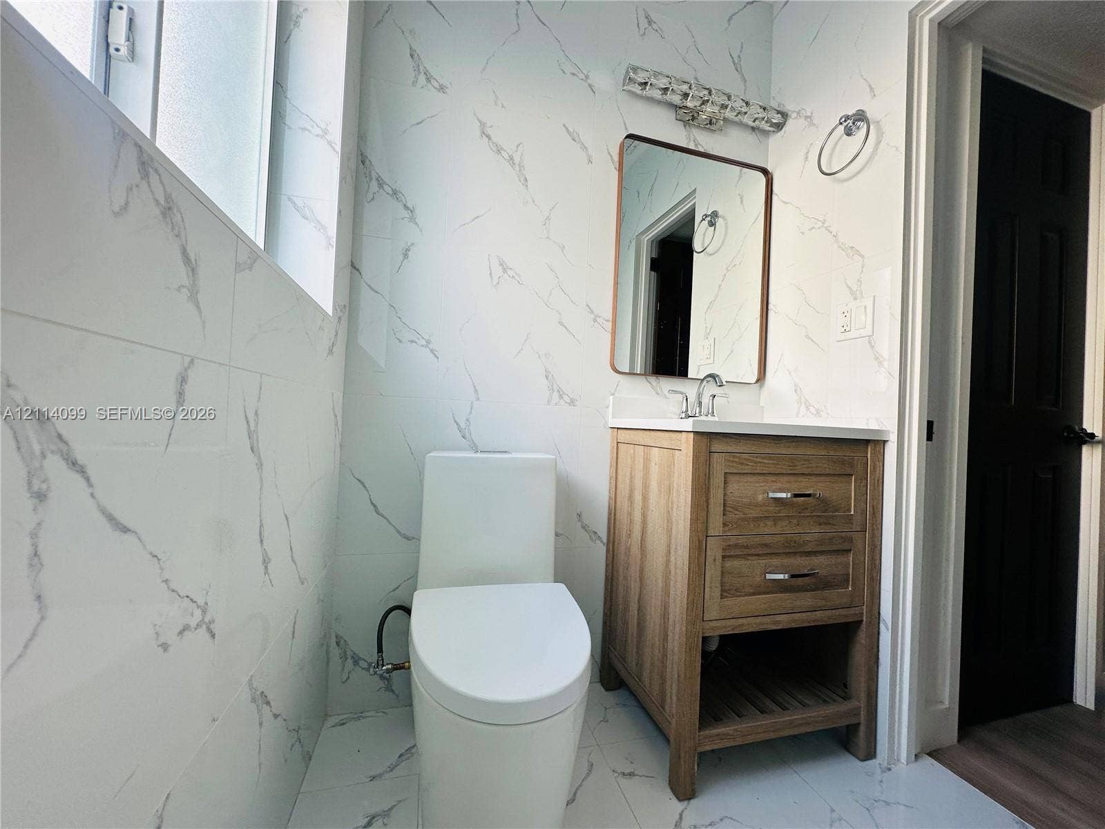 3052 SW 6th Street, Miami, FL 33135 Bathroom featuring floor-to-ceiling stone-finish wall tile, wood-finish vanity with a rectangular sink, wall-mounted rectangular mirror, and modern elongated toilet