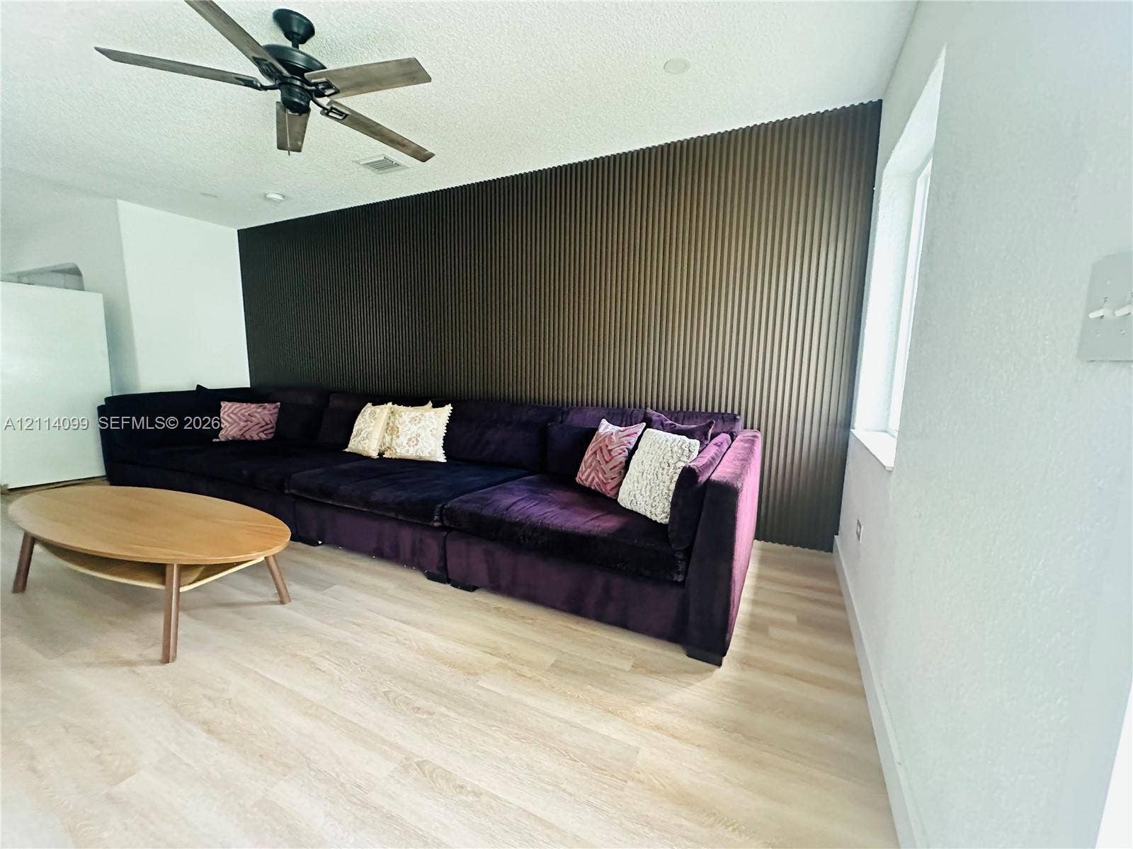 3052 SW 6th Street, Miami, FL 33135 Accent wall with vertical fluted paneling, light-tone wood-finish flooring, and a multi-blade ceiling fan