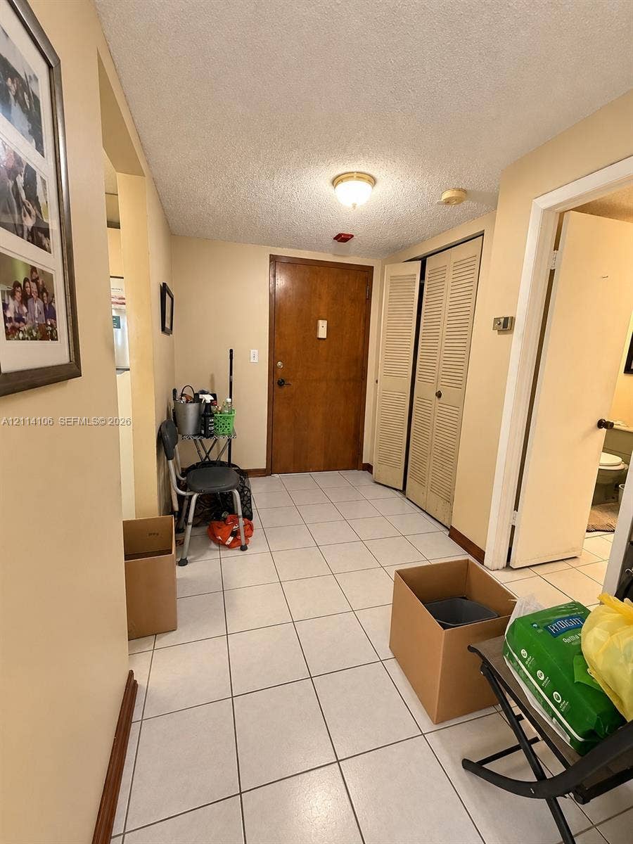 8990 SW 24th Street, #214, Miami, FL 33165 Entryway featuring ceramic tile flooring, solid wood-finish entry door, and bi-fold closet doors with louvered panels