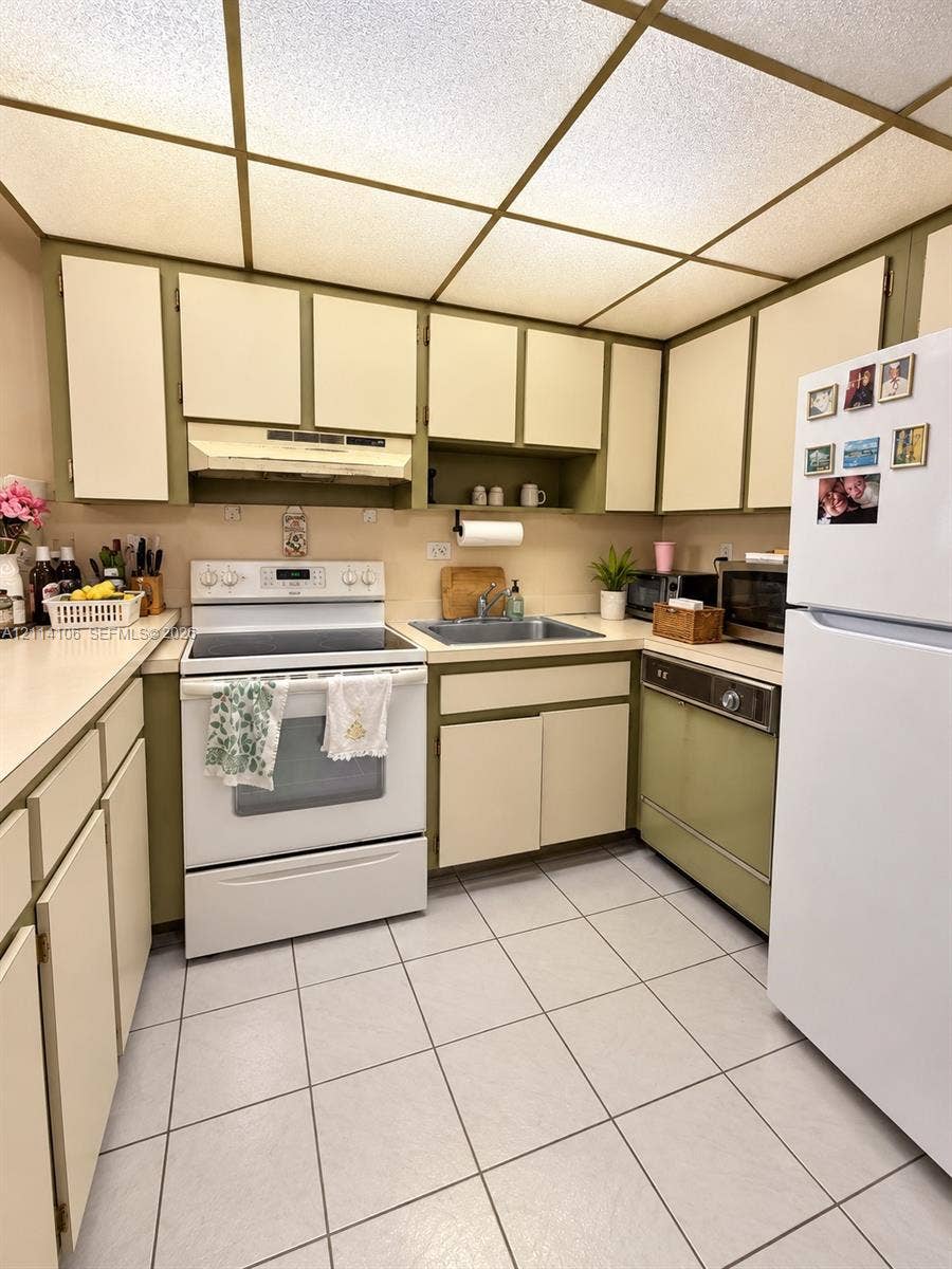8990 SW 24th Street, #214, Miami, FL 33165 Kitchen featuring flat-panel cabinetry, a dual-basin stainless steel sink, a drop-ceiling grid with integrated lighting, and ceramic tile flooring