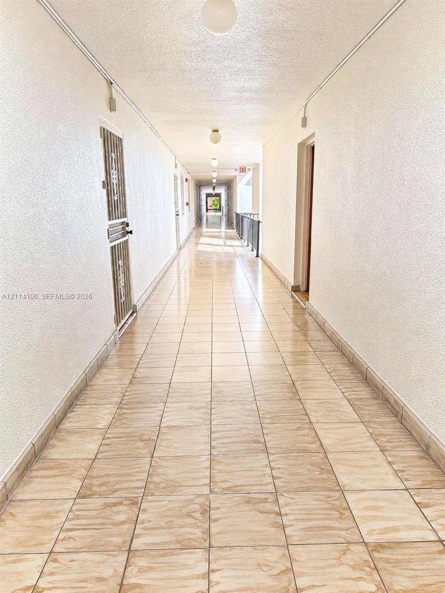 8990 SW 24th Street, #214, Miami, FL 33165 Hallway featuring ceramic tile flooring, textured wall finishes, and flush-mount ceiling lighting