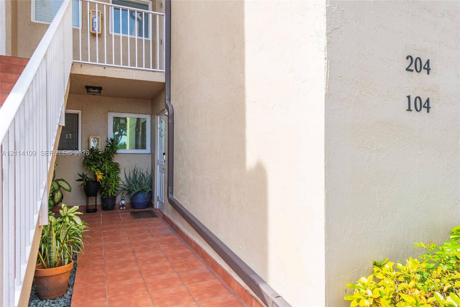 15761 SW 137th Avenue, #104, Miami, Miami, FL 33177 Stucco exterior featuring terracotta-style tile flooring, white metal staircase railings, and integrated external lighting fixtures
