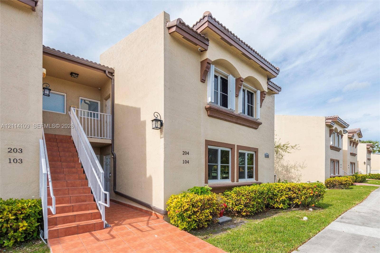 15761 SW 137th Avenue, #104, Miami, Miami, FL 33177 Stucco exterior featuring arched window details, terracotta-tiled staircase, metal railings, and attached wall-mounted lantern-style lighting