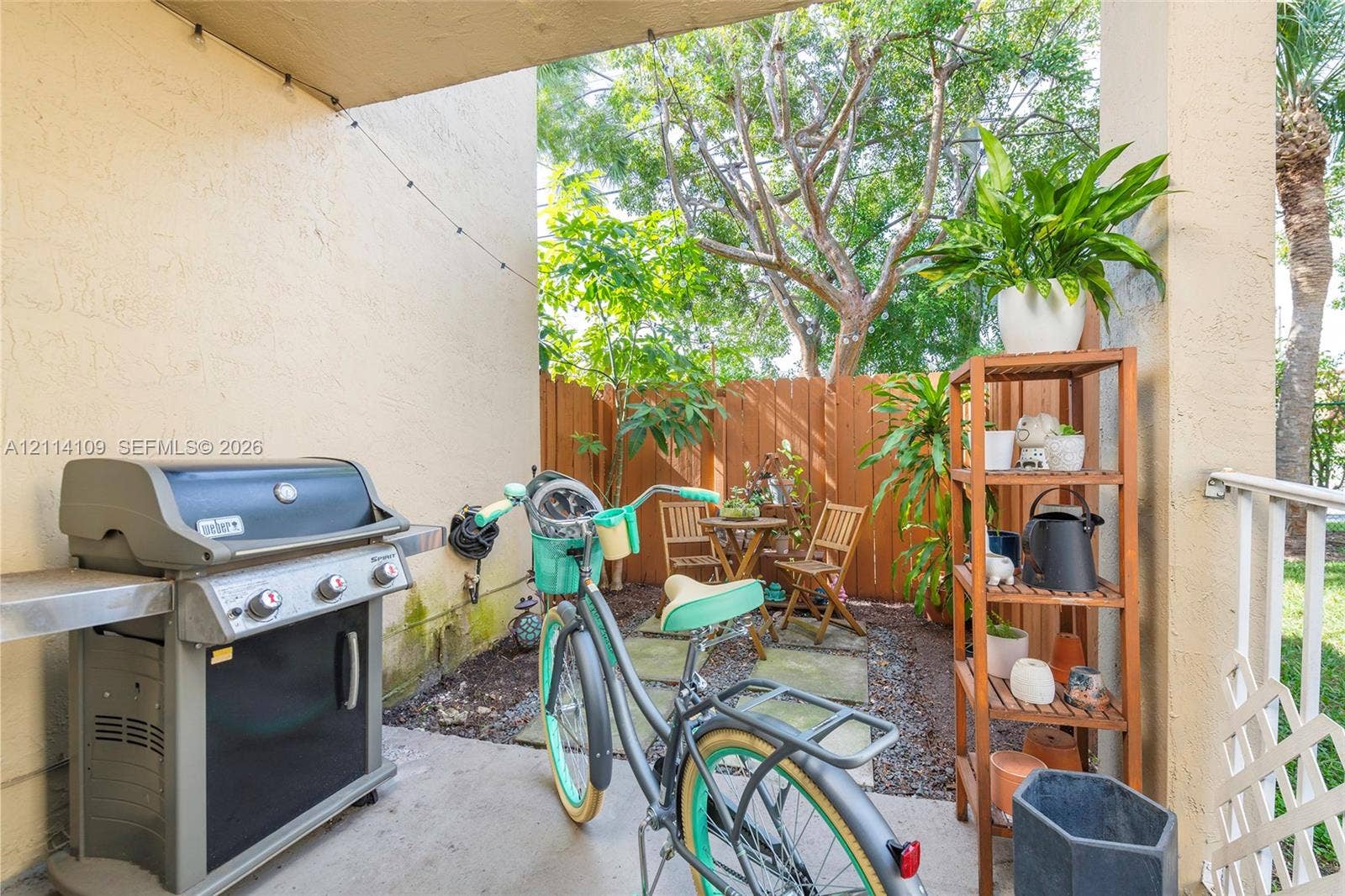 15761 SW 137th Avenue, #104, Miami, Miami, FL 33177 Covered concrete patio featuring a perimeter wood privacy fence, stone paver accents, and mature tree landscaping
