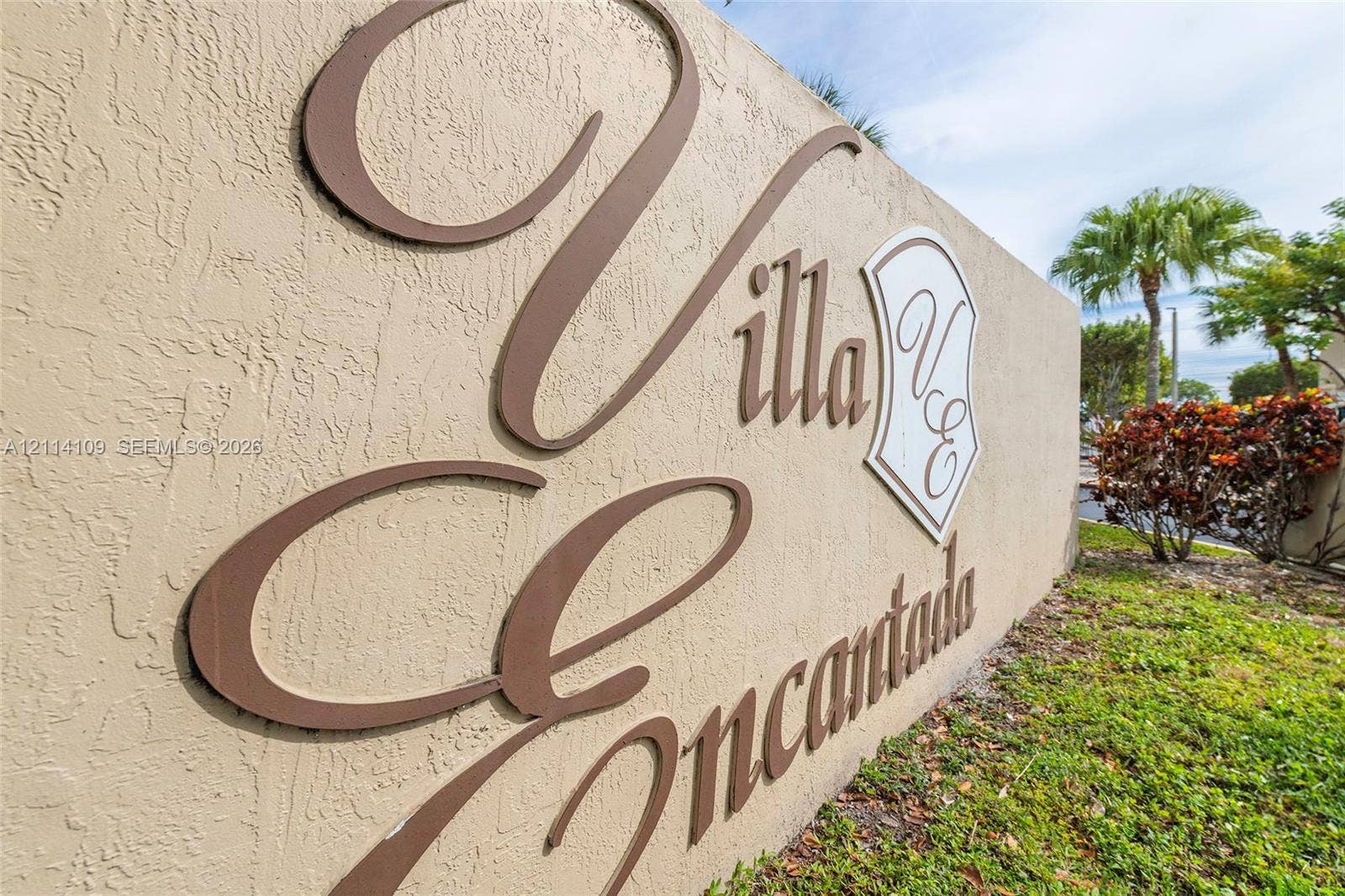 15761 SW 137th Avenue, #104, Miami, Miami, FL 33177 Textured stucco monument signage featuring dimensional metal lettering and a decorative emblem, accented by professional landscaping with palm trees and shrubbery