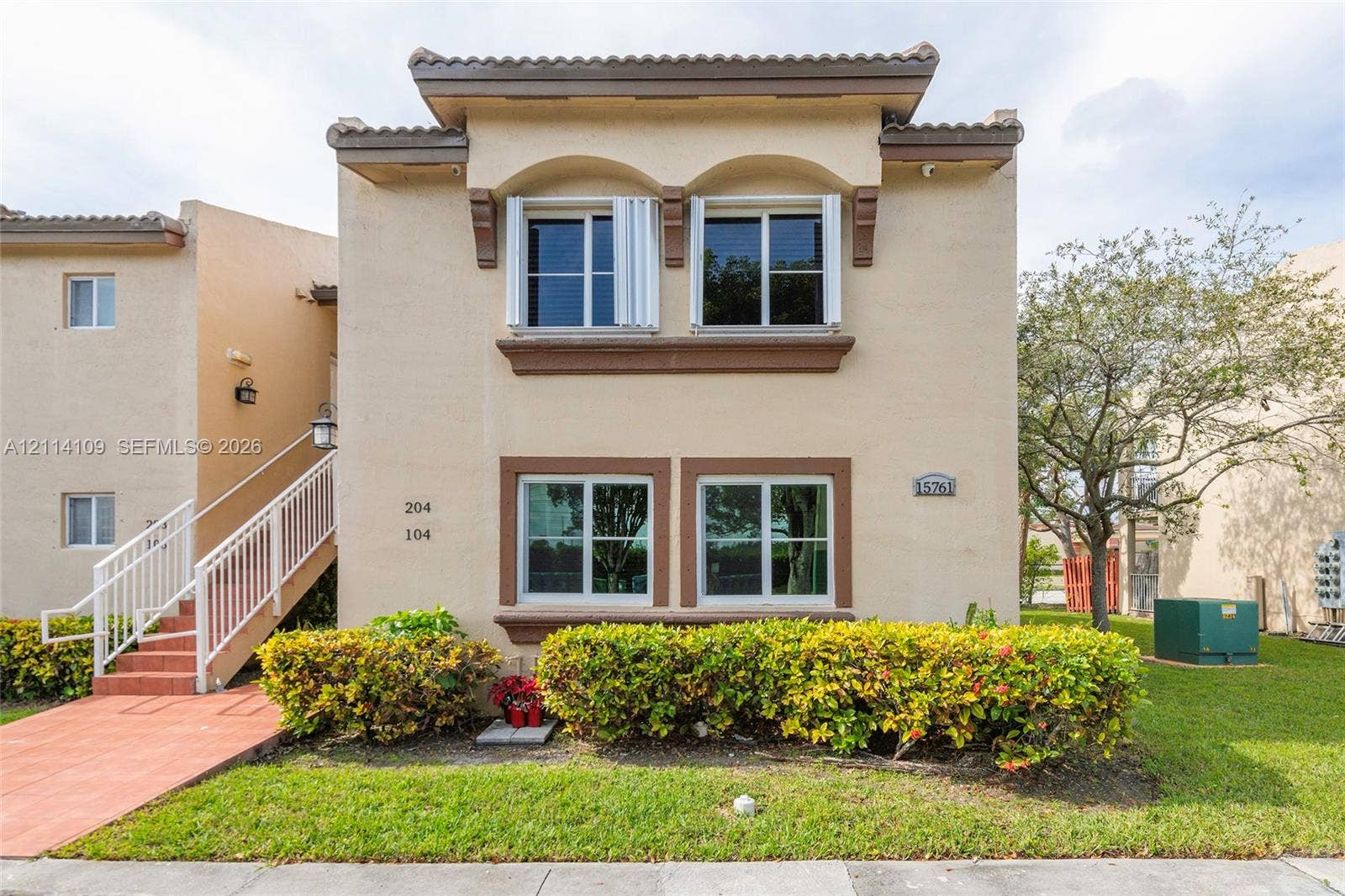 15761 SW 137th Avenue, #104, Miami, Miami, FL 33177 Stucco exterior featuring dual-level arched window accents, tile roof trim, and an exterior staircase with white metal railings