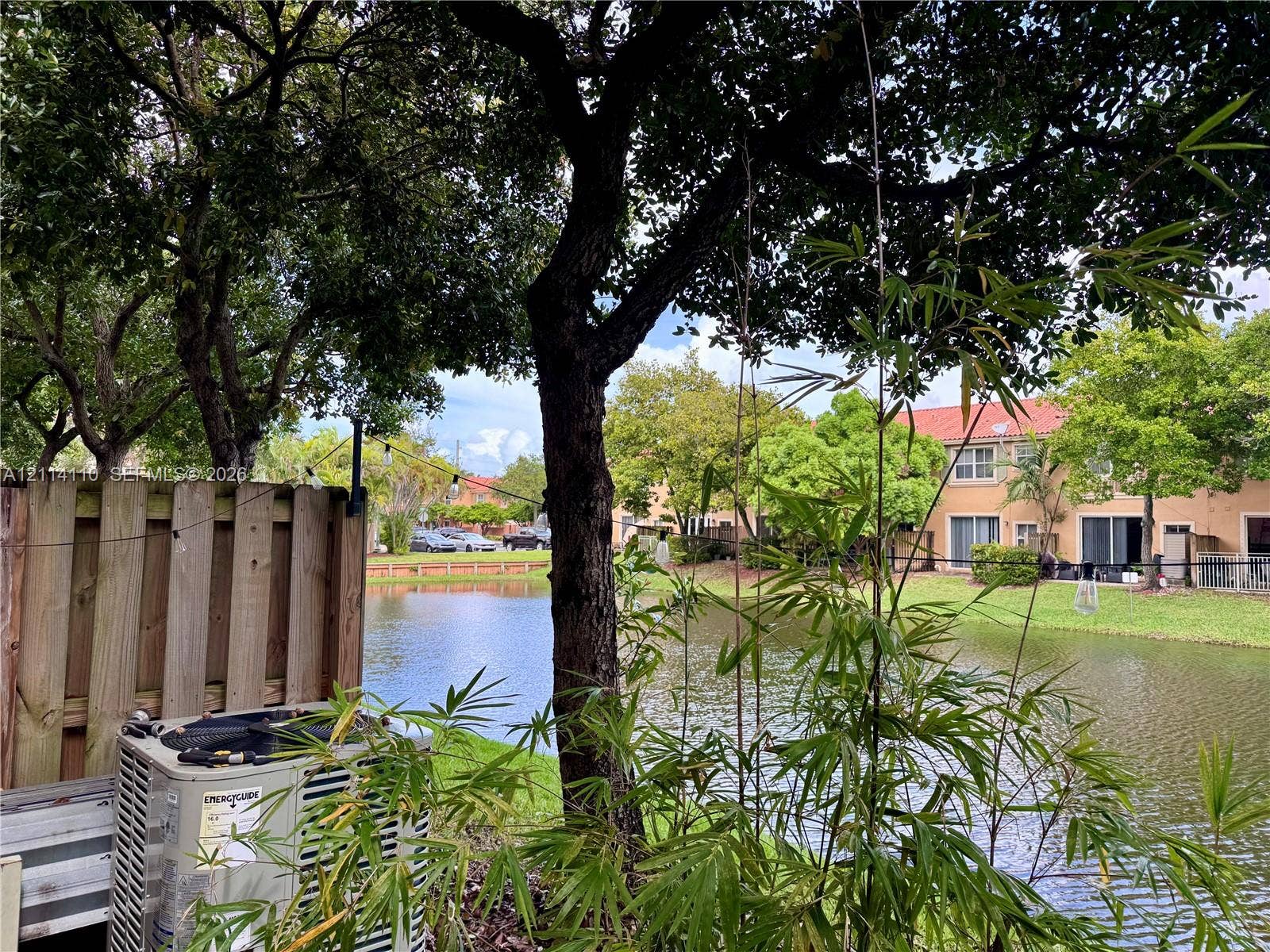 4928 Leeward Lane, #3603, Dania Beach, FL 33312 Waterfront lot featuring mature trees, a wood-slatted privacy fence, and native vegetation