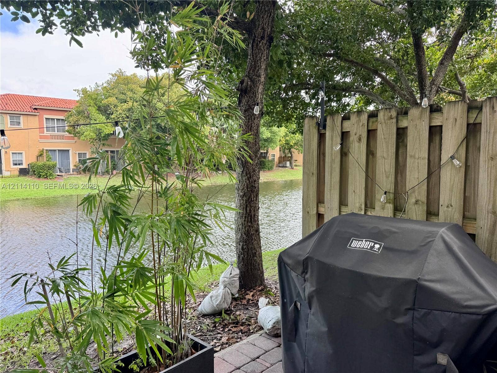 4928 Leeward Lane, #3603, Dania Beach, FL 33312 Waterfront patio featuring paver hardscaping, mature trees, and a wooden privacy fence