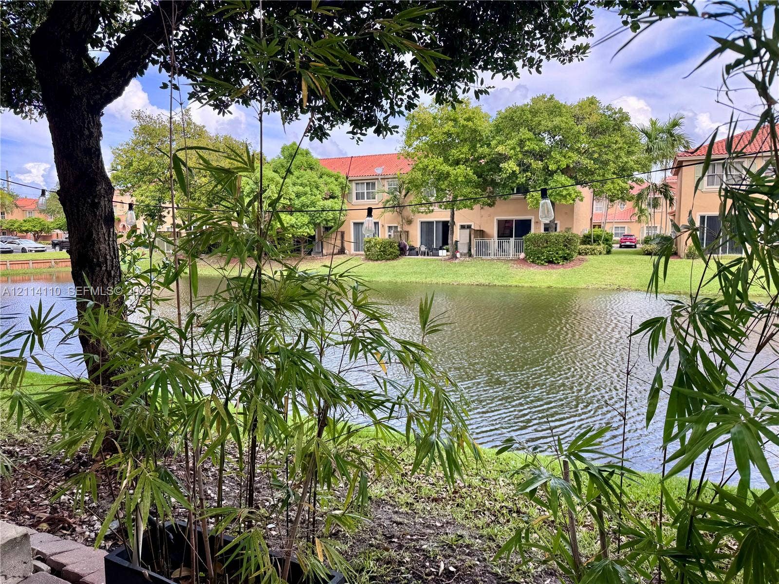 4928 Leeward Lane, #3603, Dania Beach, FL 33312 Waterfront grounds featuring a pond, mature trees, manicured lawn, and terracotta-style roof tiles