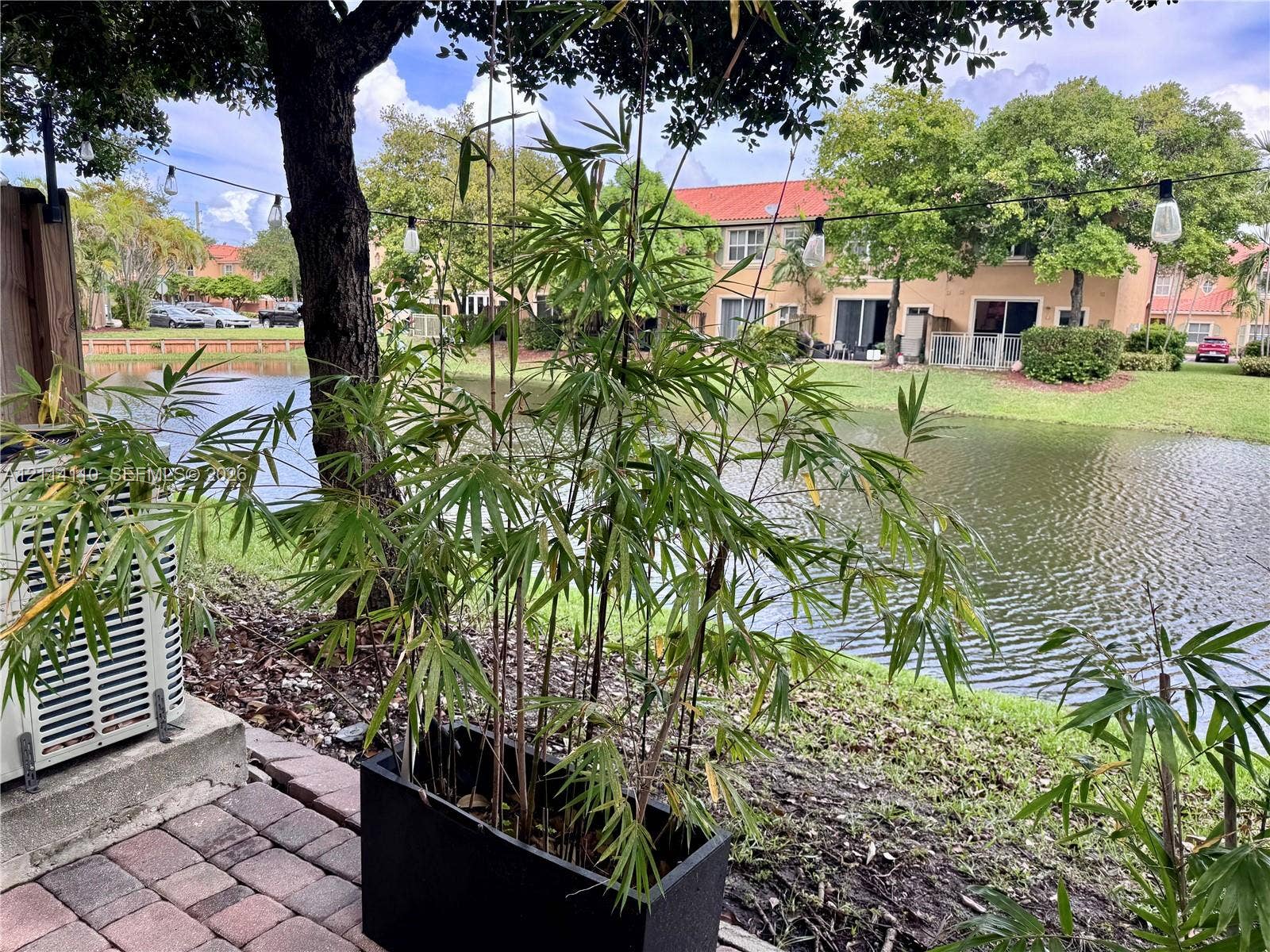 4928 Leeward Lane, #3603, Dania Beach, FL 33312 Paver patio featuring water frontage, mature landscaping, and an installed exterior string lighting system