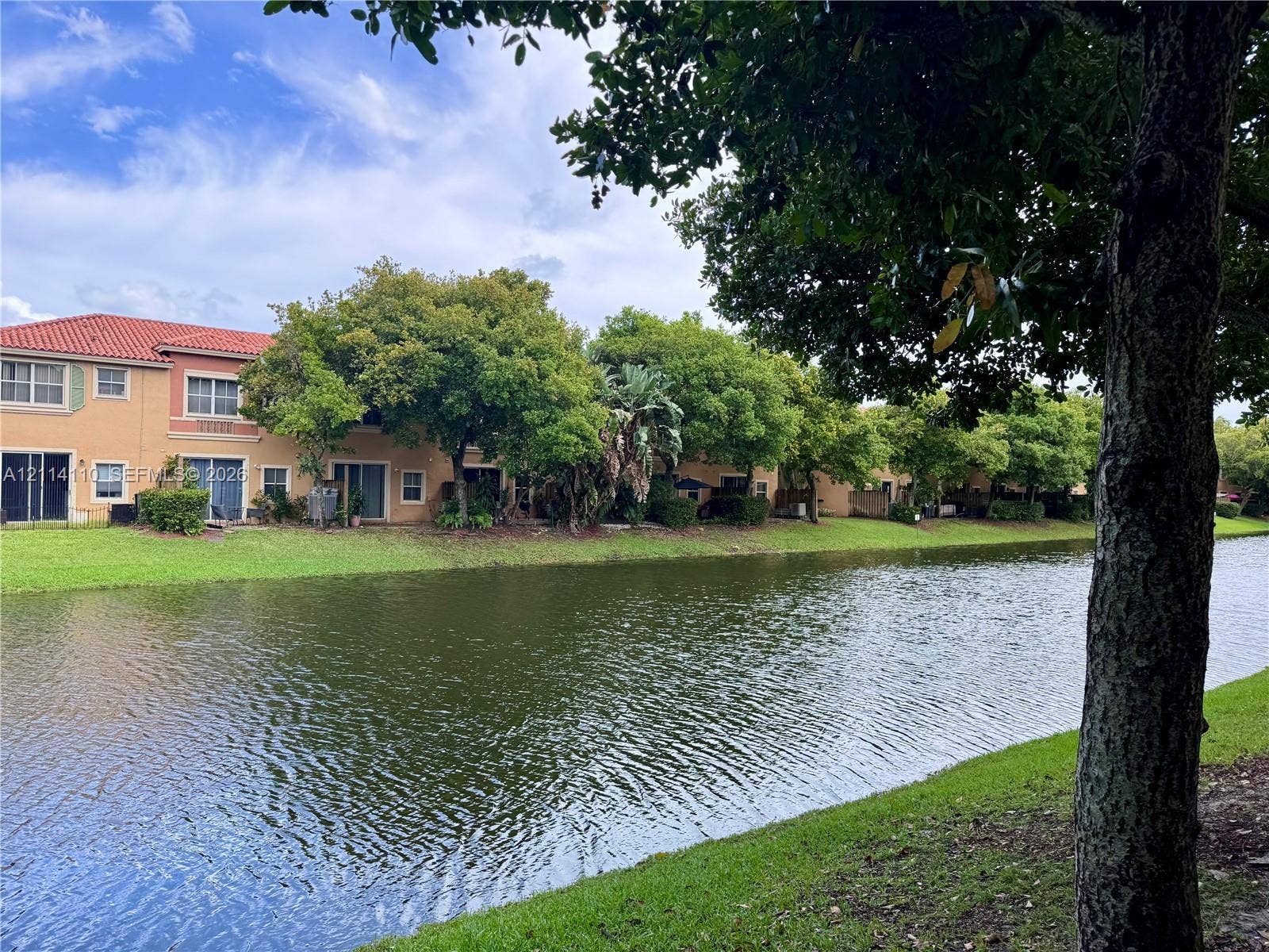 4928 Leeward Lane, #3603, Dania Beach, FL 33312 Waterfront exterior featuring a terracotta-tile roof, stucco facade, sliding glass doors, and expansive green space with mature trees