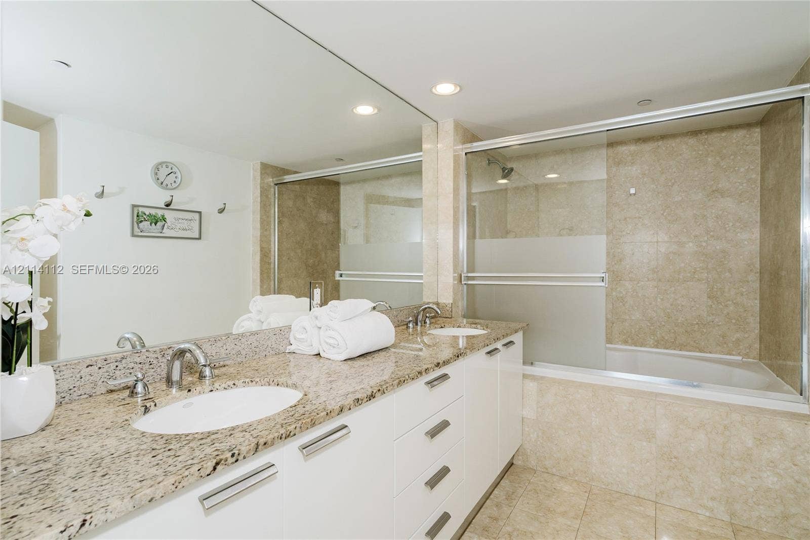 1850 S Ocean Drive, #4008, Hallandale Beach, FL 33009 Full-width vanity with stone countertop, dual undermount sinks, contemporary white cabinetry, and tub-shower combination featuring sliding glass doors and tiled surround