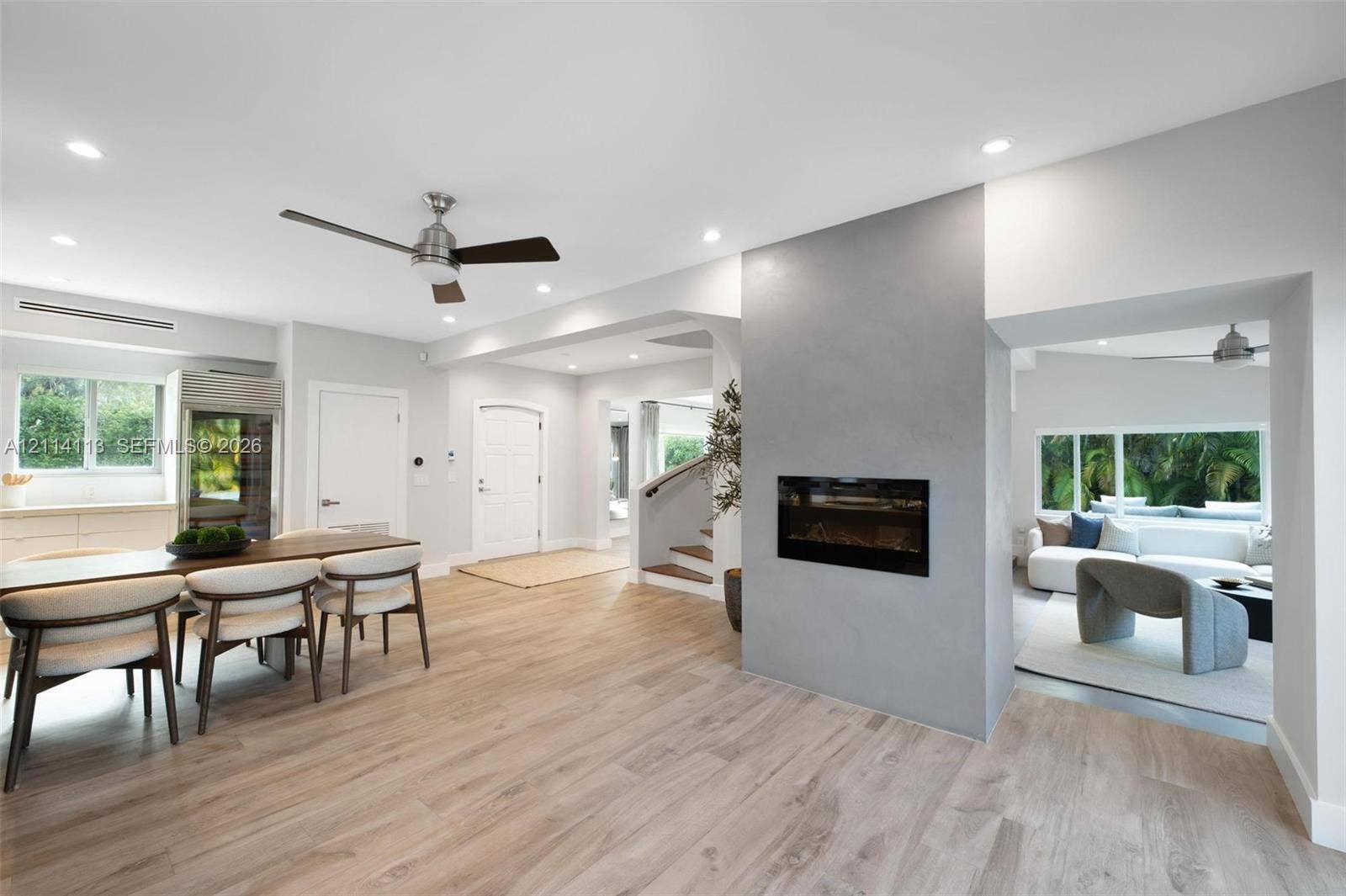 5386 Alton Road, Miami Beach, FL 33140 Light-toned wood-finish flooring, central fireplace with a grey smooth-finish surround, recessed ceiling lighting, ceiling fans, and multi-paned windows