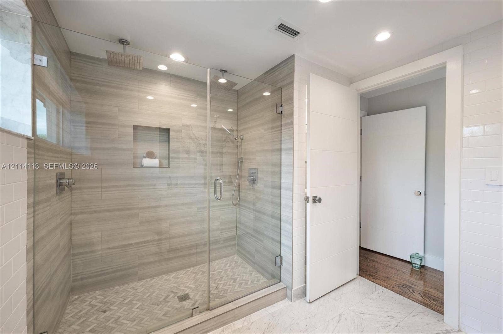 5386 Alton Road, Miami Beach, FL 33140 Walk-in shower featuring glass enclosure, ceiling-mounted rainfall showerhead, integrated tiled wall niche, and herringbone-patterned floor tile