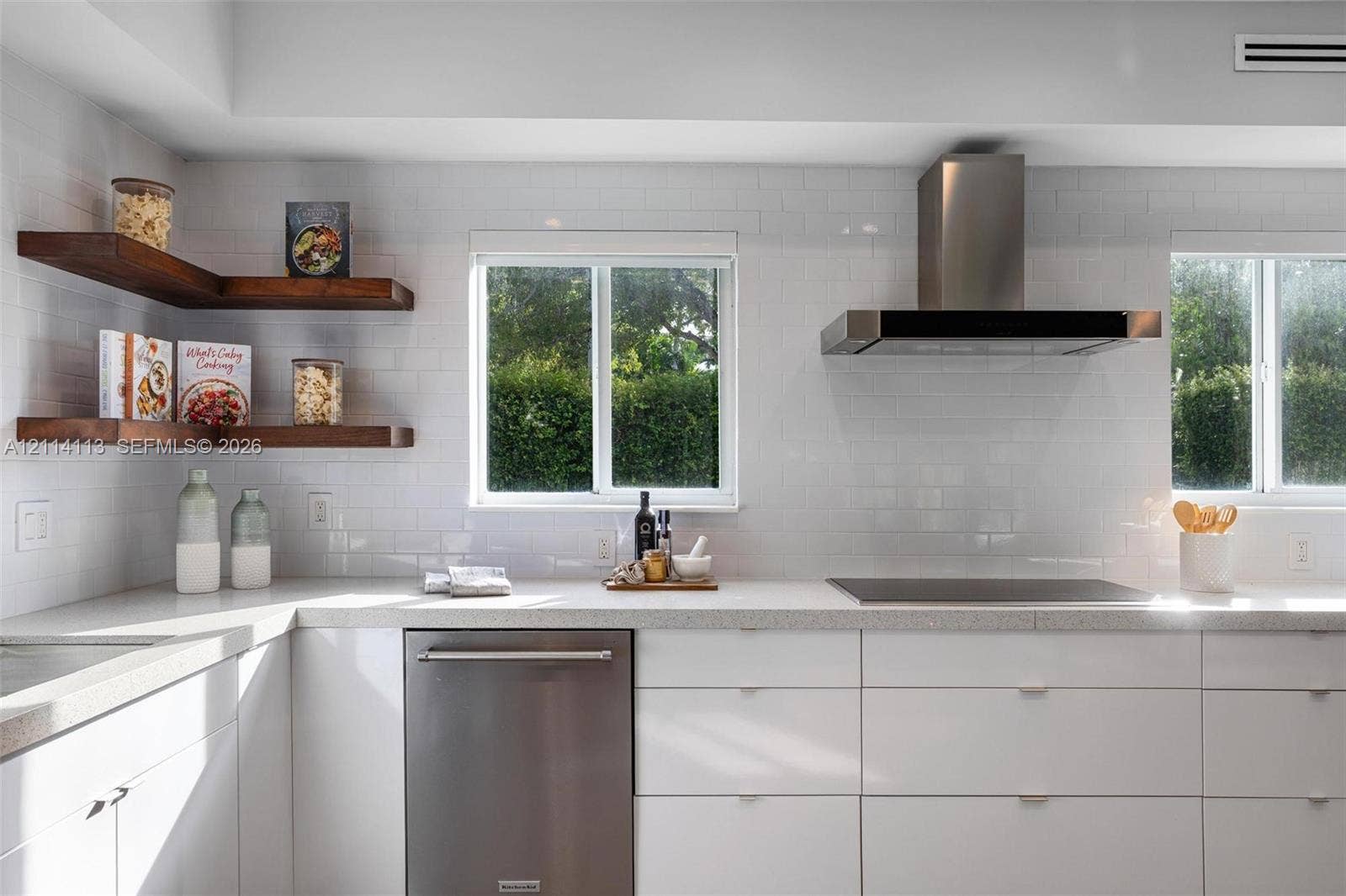 5386 Alton Road, Miami Beach, FL 33140 Kitchen featuring white flat-panel cabinetry, stone countertops, stainless steel appliances, a stainless steel range hood, and wood-finish floating corner shelves