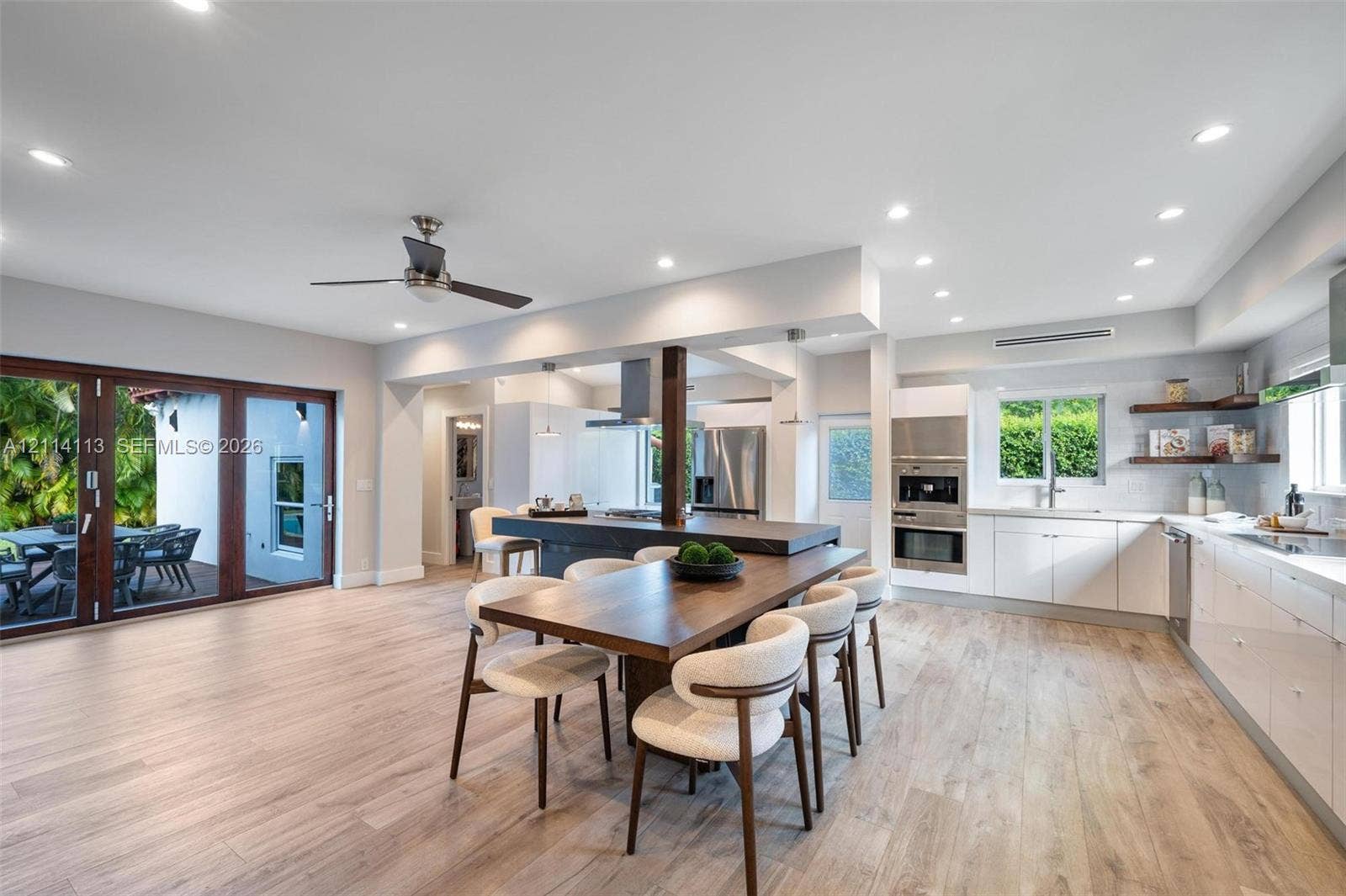 5386 Alton Road, Miami Beach, FL 33140 Open-concept kitchen, white cabinetry, recessed lighting, stainless steel wall ovens, and multi-panel glass doors