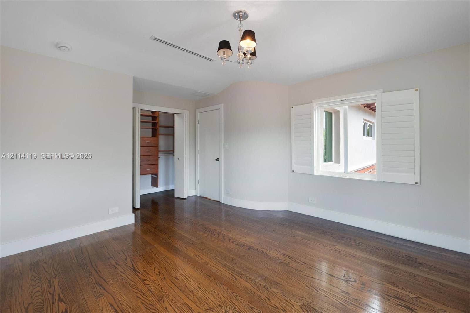 5386 Alton Road, Miami Beach, FL 33140 Room featuring wood-finish flooring, white plantation shutters, a multi-light chandelier, and a walk-in closet with built-in wooden shelving and drawers