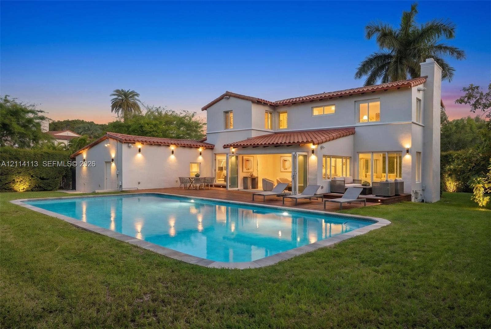 5386 Alton Road, Miami Beach, FL 33140 Two-story stucco exterior with a clay tile roof, oversized swimming pool, wood-finish decking, and multi-panel folding glass doors