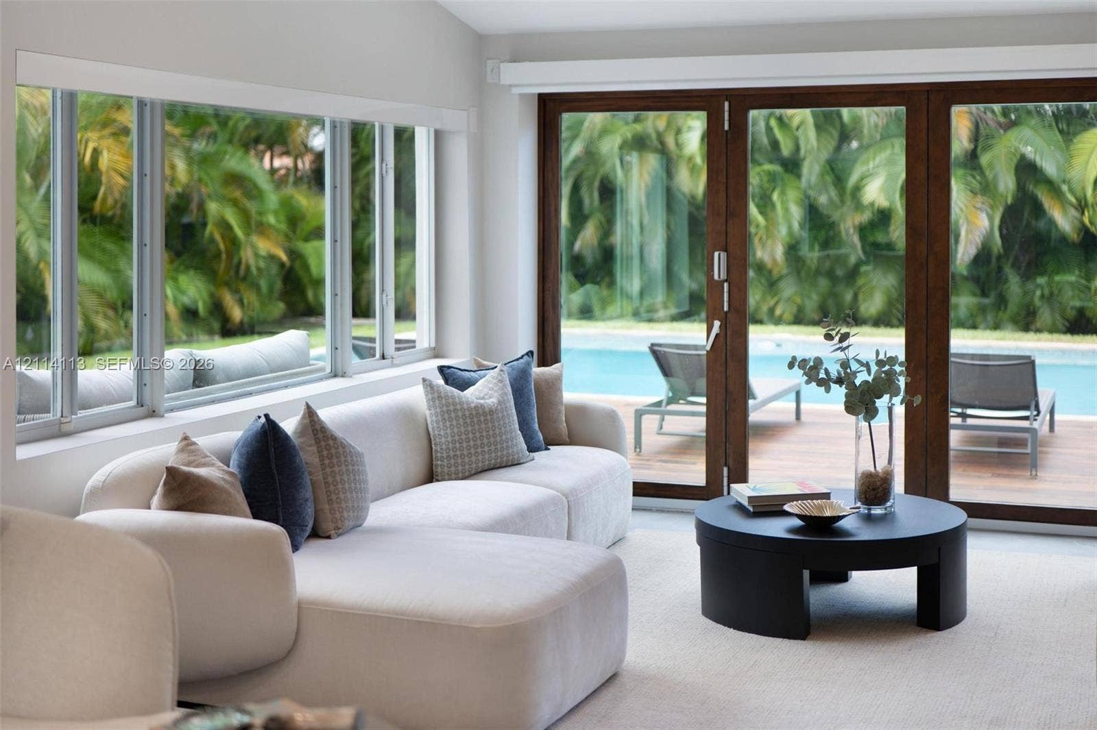 5386 Alton Road, Miami Beach, FL 33140 Expansive multi-pane windows and large-format sliding glass doors with dark wood frames, offering visibility to the outdoor pool and lush foliage