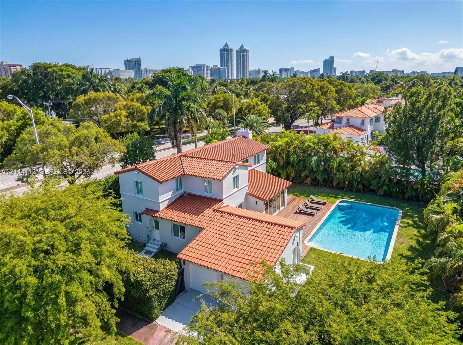 5386 Alton Road, Miami Beach, FL 33140 Two-story residence featuring a terracotta-tiled roof, rectangular swimming pool, wood-decking patio, and manicured landscaping