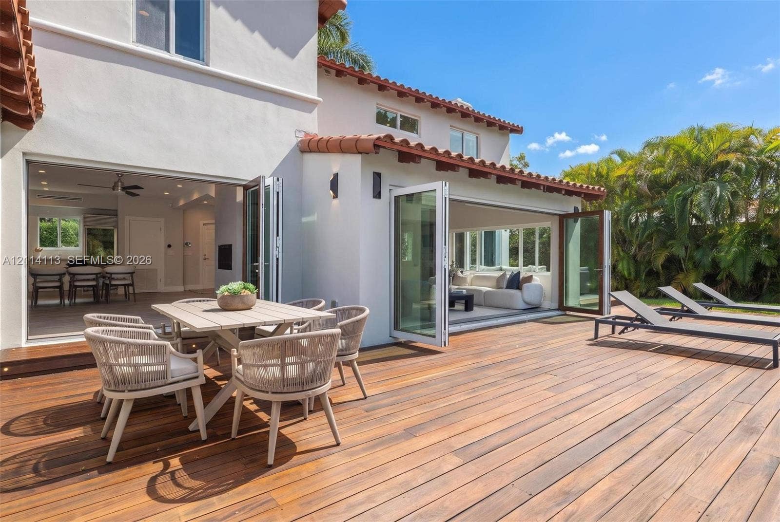 5386 Alton Road, Miami Beach, FL 33140 Expansive wood-finish deck with integrated bi-fold glass doors, white stucco exterior, and terracotta tile roofing