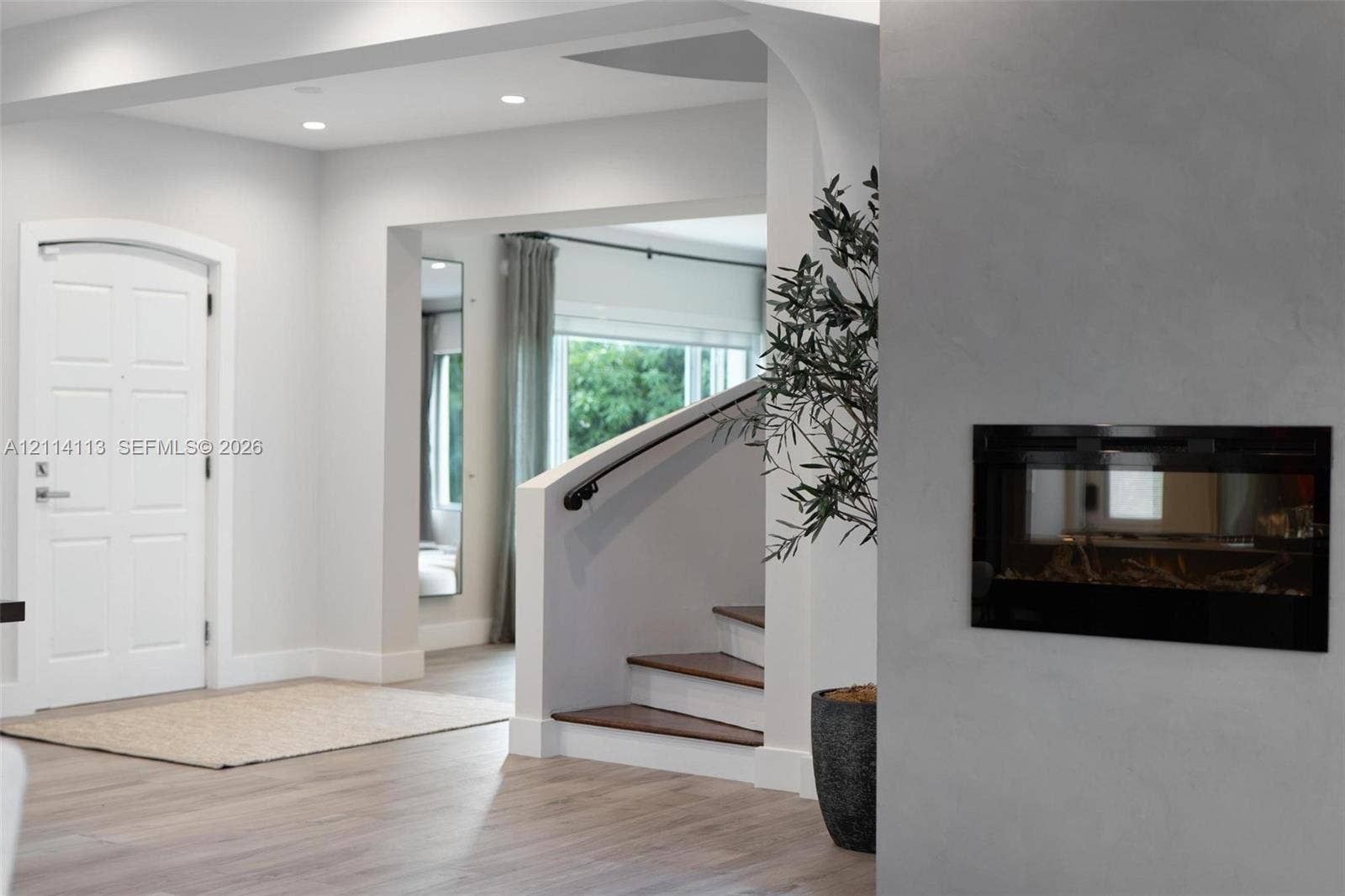 5386 Alton Road, Miami Beach, FL 33140 Foyer featuring recessed lighting, a recessed wall-mounted fireplace, a white arched-top entry door, and a staircase with wood-finish treads and a matte black handrail