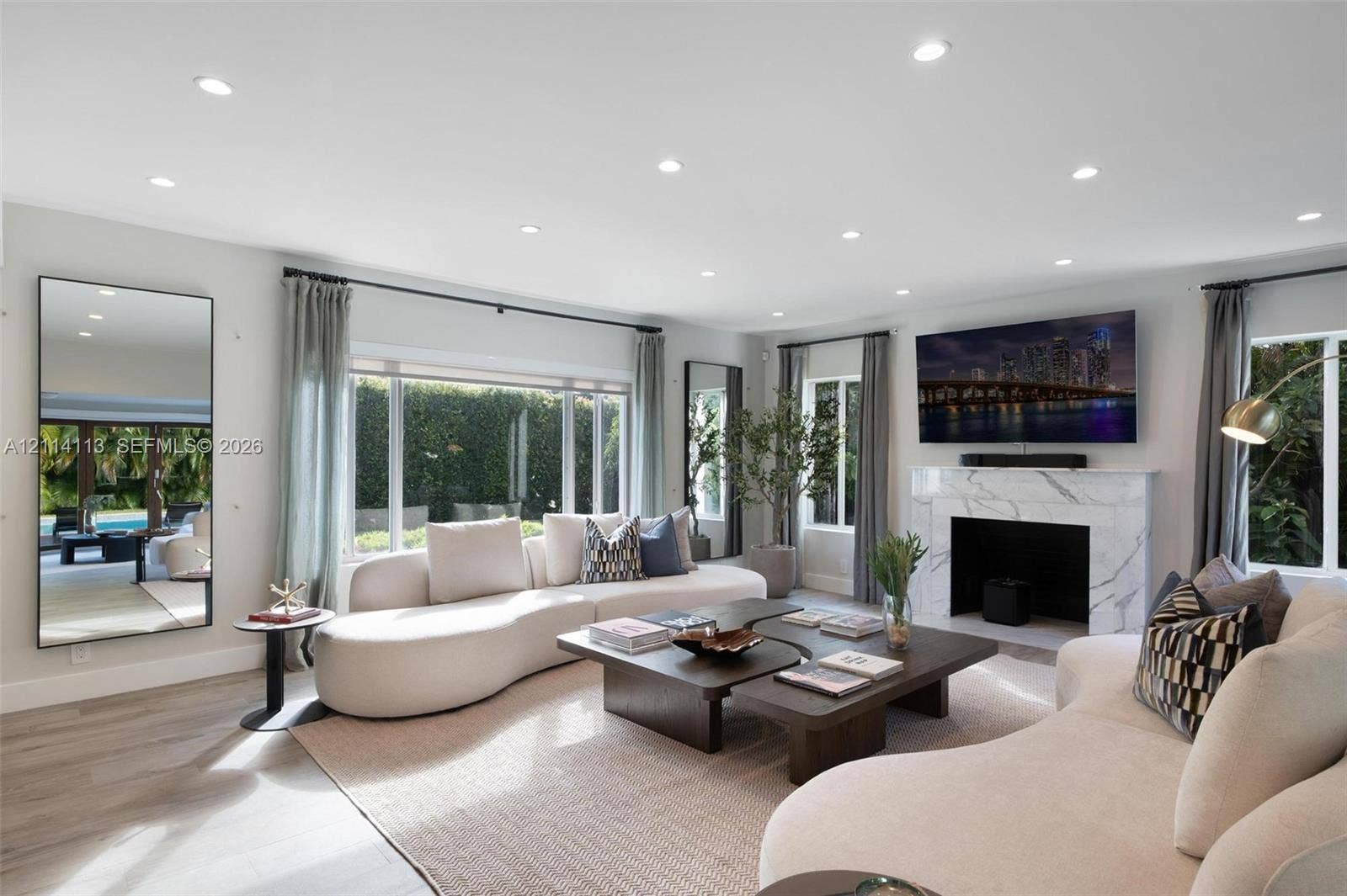 5386 Alton Road, Miami Beach, FL 33140 Spacious interior filled with natural light, featuring recessed lighting, stone-finish fireplace surround, large-format windows, and wood-finish porcelain flooring
