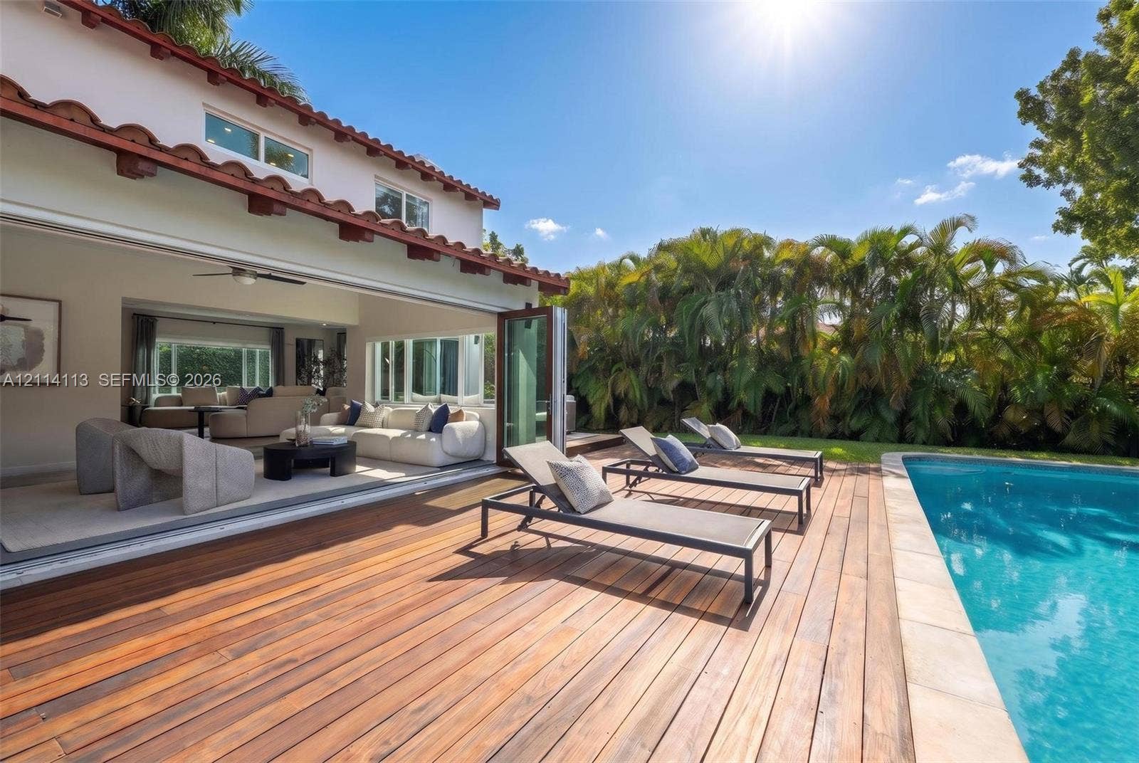 5386 Alton Road, Miami Beach, FL 33140 Outdoor space featuring a wood-plank deck, built-in swimming pool, terracotta-tiled roofline, and multi-panel folding glass doors