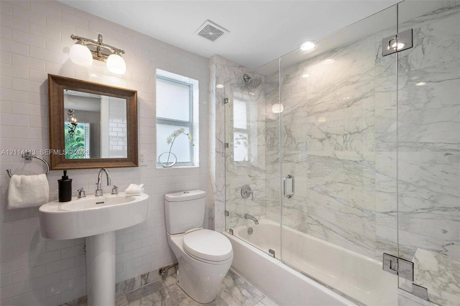 5386 Alton Road, Miami Beach, FL 33140 Full bathroom featuring a white porcelain pedestal sink, stone-patterned wall-to-wall shower surround with a frameless glass door, stone-patterned tile flooring, subway-tiled walls