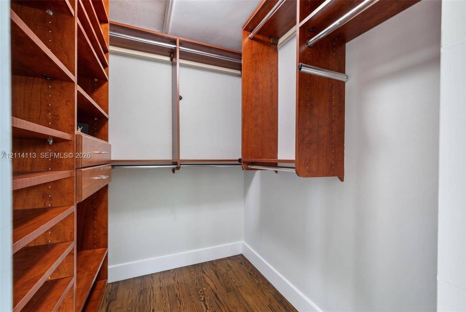 5386 Alton Road, Miami Beach, FL 33140 Walk-in closet featuring custom wood-finish shelving, integrated drawers, metal hanging rods, and wood-finish flooring