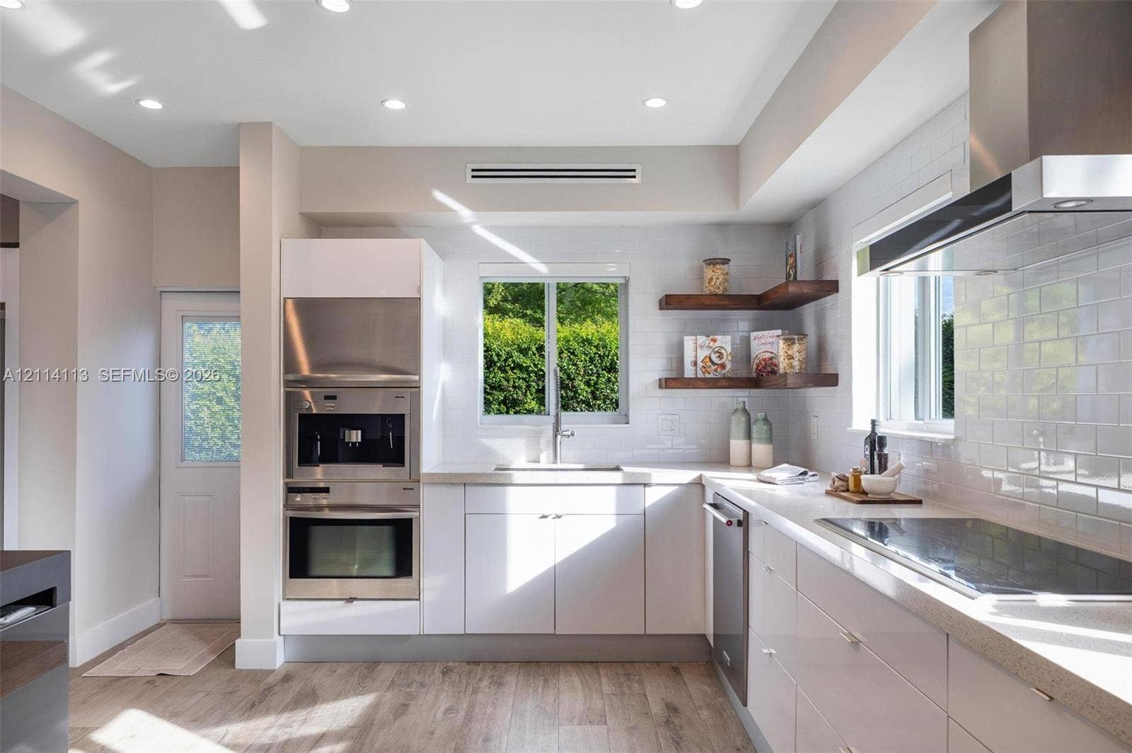 5386 Alton Road, Miami Beach, FL 33140 Kitchen featuring white cabinetry, wood-finish flooring, subway tile backsplash, stainless steel built-in appliances, and floating wood shelving