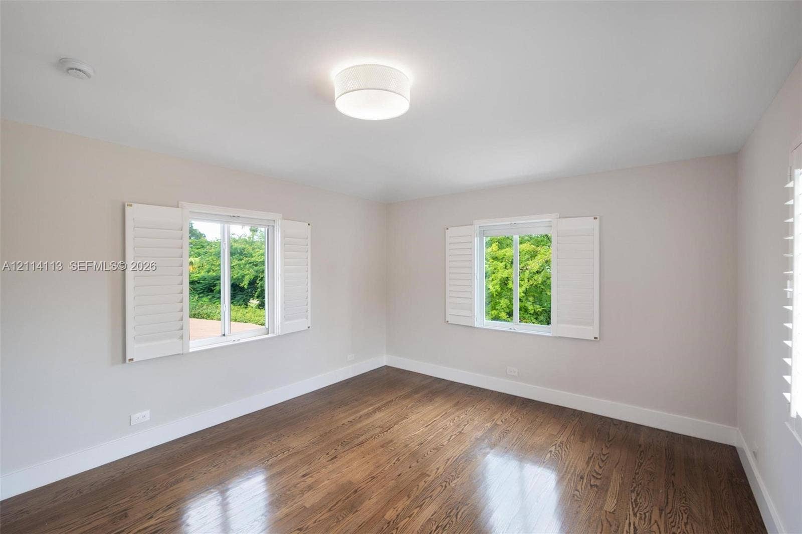 5386 Alton Road, Miami Beach, FL 33140 Neutral interior featuring wood-finish flooring, white plantation shutters, and a central drum flush-mount light fixture
