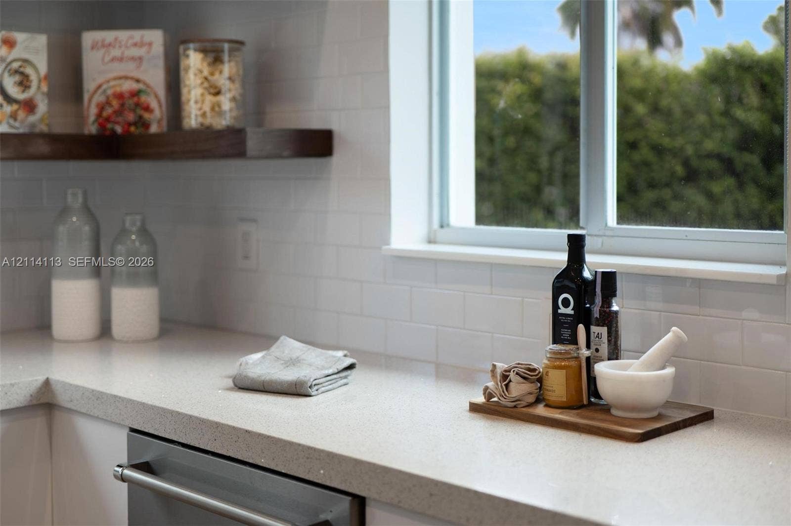 5386 Alton Road, Miami Beach, FL 33140 Kitchen featuring light-toned solid surface countertops, white subway tile backsplash, stainless steel dishwasher, and floating wood-finish shelving