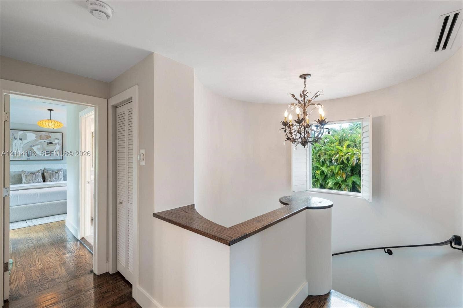 5386 Alton Road, Miami Beach, FL 33140 Curved architectural wall featuring a dark wood-finish cap, wrought-iron style chandelier, louvered closet door, and wood-finish flooring
