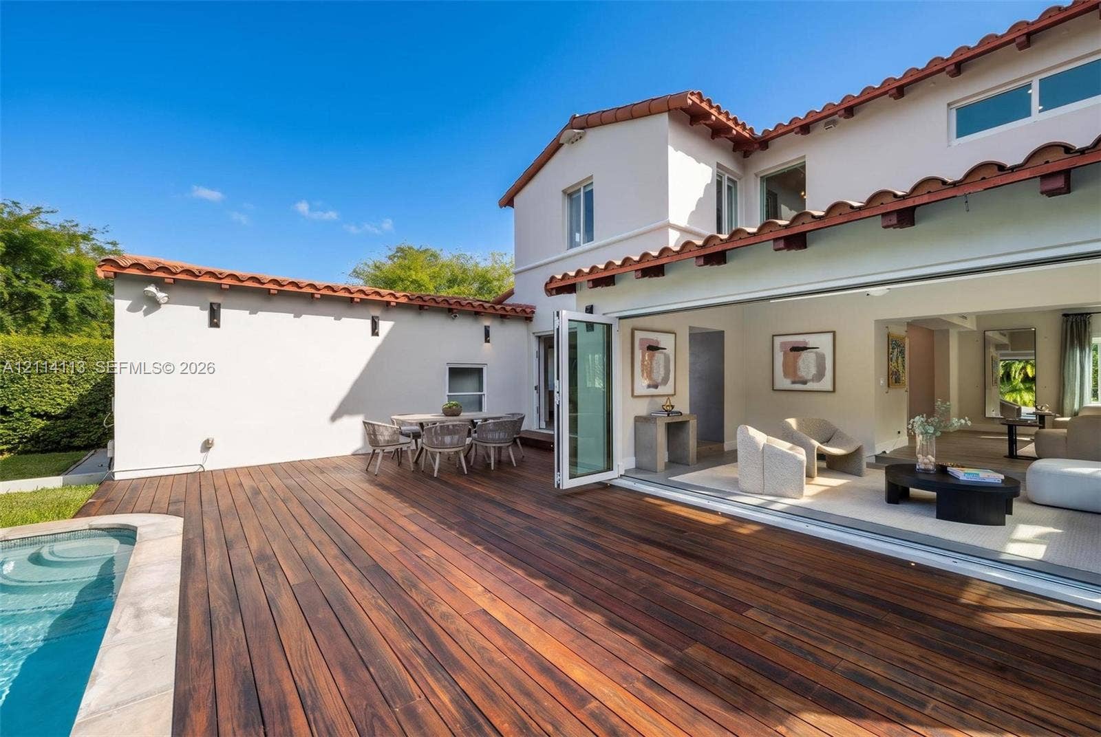 5386 Alton Road, Miami Beach, FL 33140 Spanish-style exterior featuring a terra cotta tile roof, expansive wood deck, swimming pool with stone coping, and large-format bi-fold glass doors