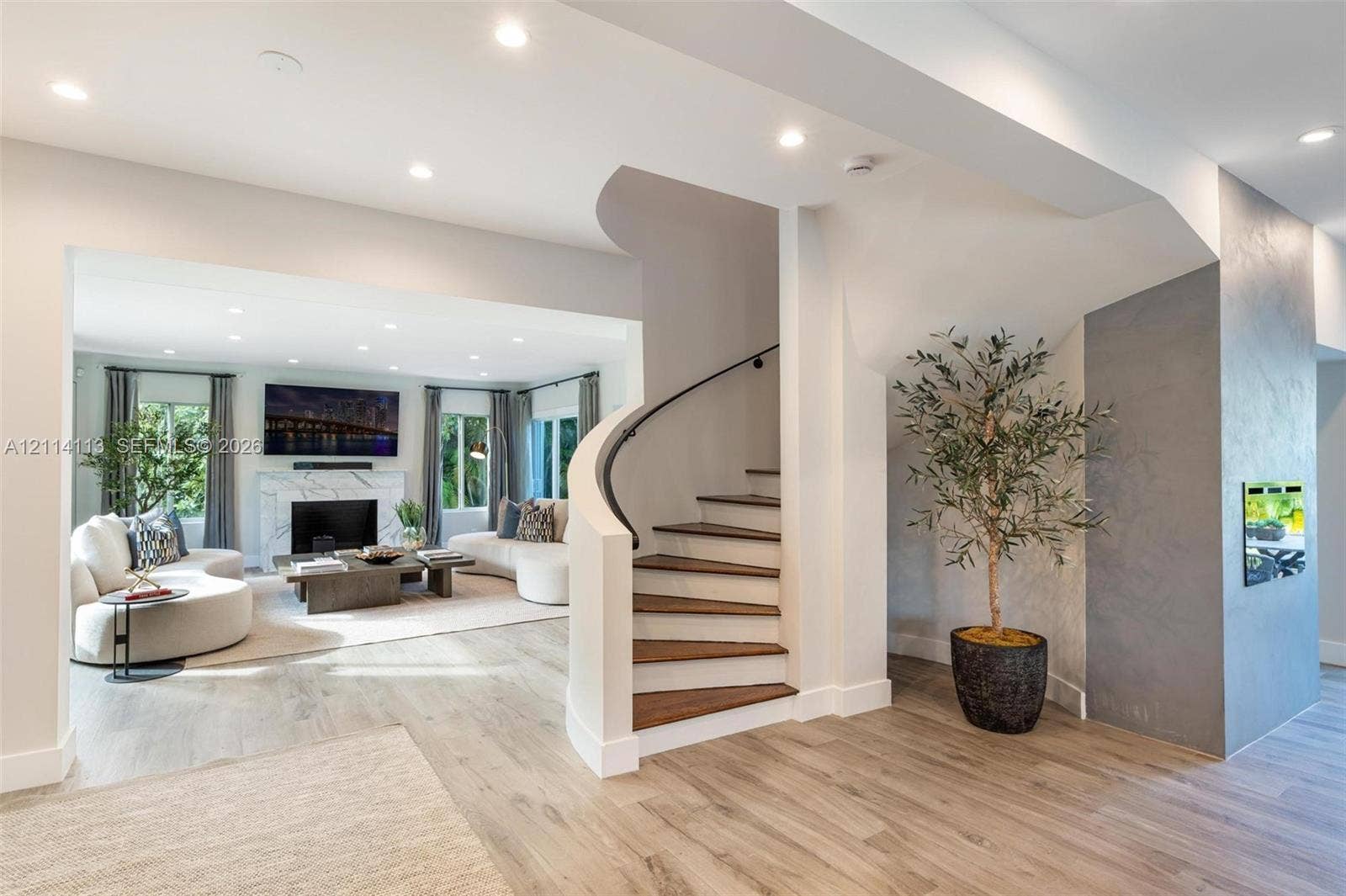 5386 Alton Road, Miami Beach, FL 33140 Curved staircase with wood treads and black metal handrail, fireplace with stone-surround, recessed lighting, and wood flooring