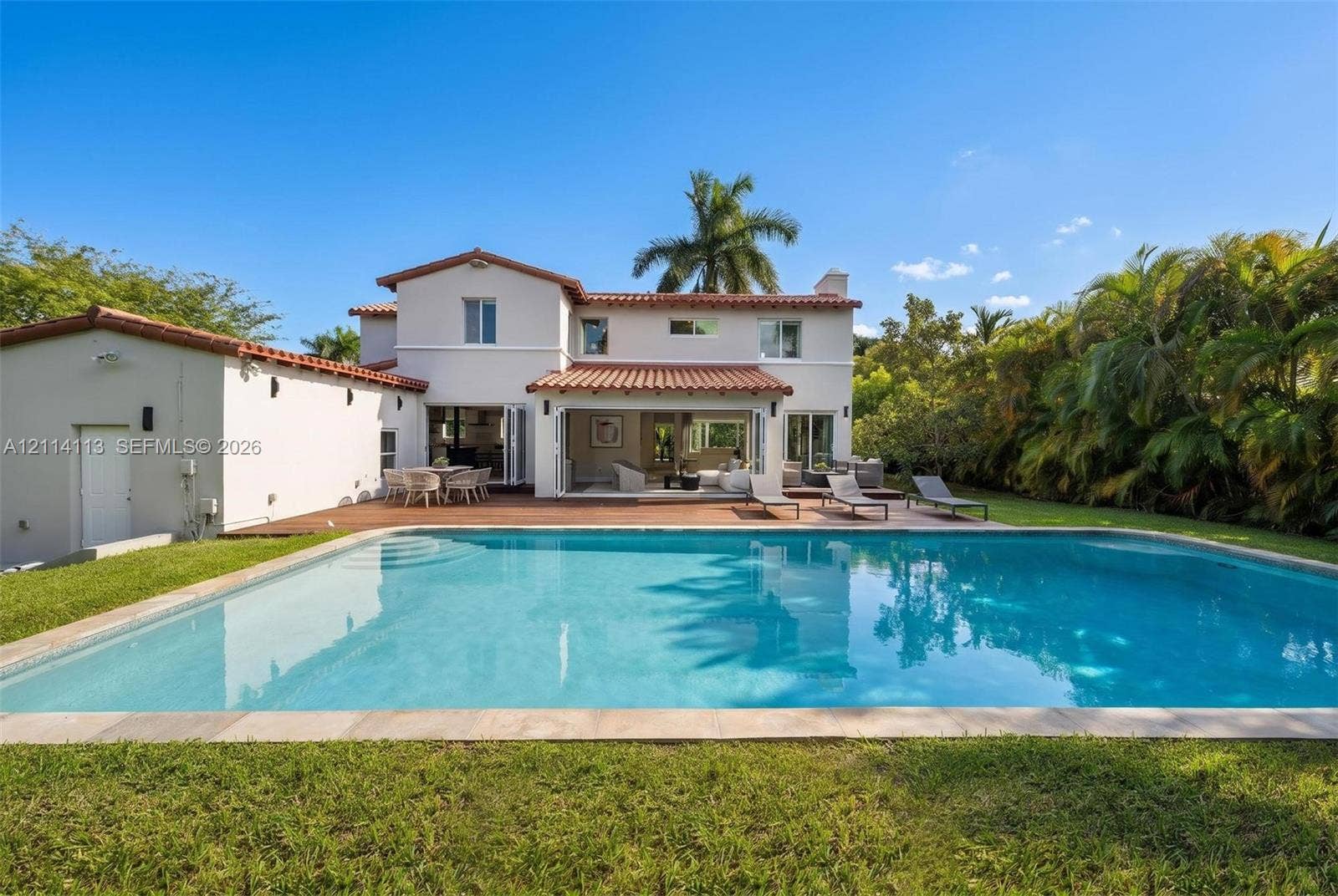 5386 Alton Road, Miami Beach, FL 33140 Two-story residence featuring a tile roof, an in-ground swimming pool, a wood-decked patio, and exterior bi-fold glass doors